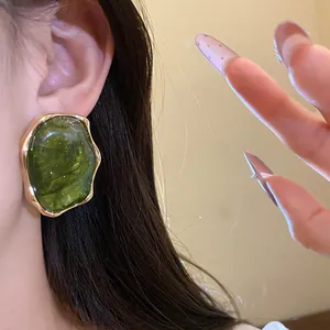 Primer plano de un pendiente de resina verde oscuro con borde dorado plisado en oreja