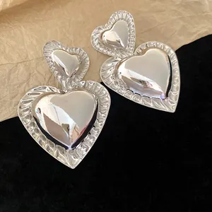 Detailed close-up view of large silver heart earrings featuring textured ridged edges and shiny finish