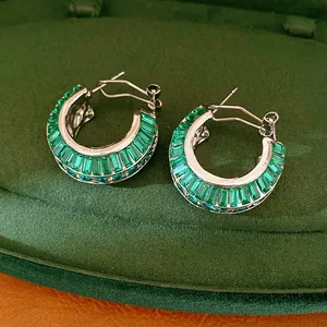 Detailed close-up view of emerald green stone hoop earrings on dark green velvet background