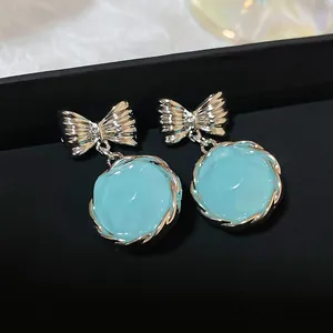 Close-up detail of elegant silver bow-tie earrings featuring light blue circular pendants