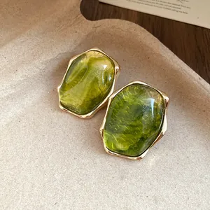 Detalle de elegantes pendientes de resina verde con bordes de metal dorado plisado vintage