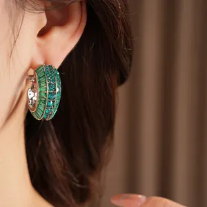 Close-up detail of silver hoop earrings set with sparkling green crystals and baguettes.