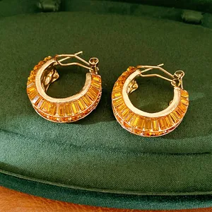 Detail of gold-plated hoop earrings featuring channel-set orange baguette crystals