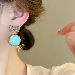 Close-up of light blue round dangling earring with silver bow knot detail
