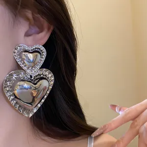 Close-up of exaggerated retro heart pendant earrings with smooth silver finish.