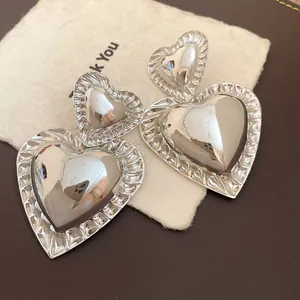Detail view of vintage silver glossy heart drop earrings with a textured ridged border.
