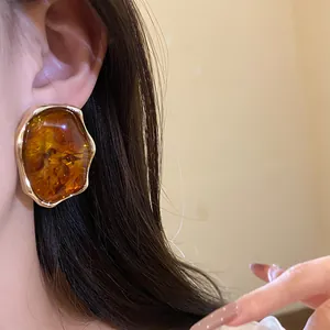 Primer plano detallado de un pendiente vintage de resina ámbar con borde dorado en la oreja