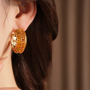 Detailed close-up of gold hoop earrings set with orange crystals on a silver needle.