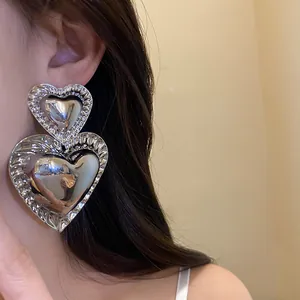 Close-up detail of oversized metallic silver double heart dangling earrings worn by a model
