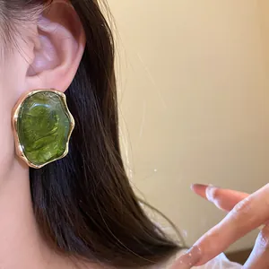 Primer plano de pendientes ovalados de resina verde vintage con borde dorado en oreja
