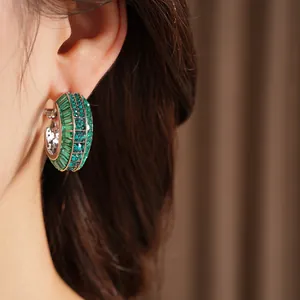 Detailed close-up of a silver hoop earring encrusted with rows of green crystals.