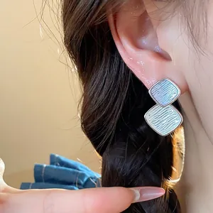 Elegante minimalistische silberfarbene Rauten-Ohrstecker mit Wellenstruktur am Modell
