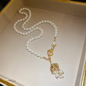 Detailansicht einer Perlenkette mit einem mit Strass besetzten Fischschwanz-Anhänger.