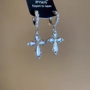Detail shot of sparkling zircon cross earrings featuring white stones on a black display card