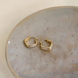 Close-up macro view of minimalist gold geometric hoop earrings with zircon stones on a tray