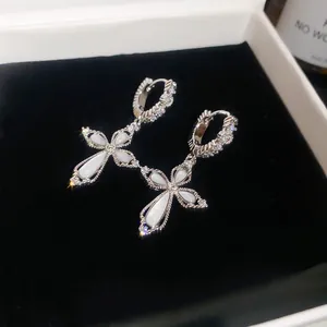 Close-up of sparkling silver cross hoop earrings with white stones and cubic zirconia.