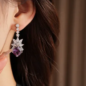 Close-up detail of silver stud earrings with purple geometric zircon and crystals