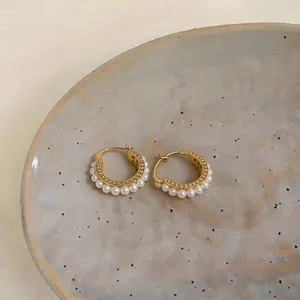 Detail of elegant gold hoop earrings with pearls and zircon on a ceramic plate.