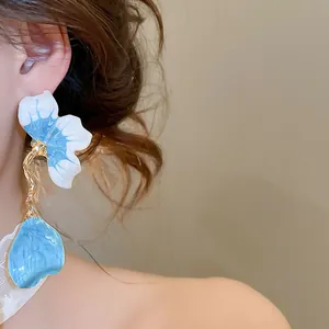 Close-up of blue and white enamel petal tassel earrings worn on a model's ear
