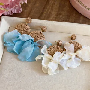 Detailed macro view of Bohemian raffia drop earrings with light blue and white chiffon flowers