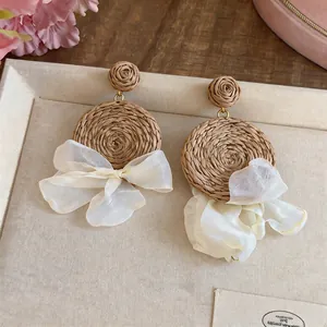 Detail of Bohemian raffia woven earrings with elegant cream chiffon bow accents