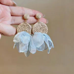 Close-up of Bohemian earrings with woven raffia and light blue chiffon petals.