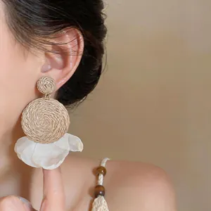 Close-up of bohemian raffia and white chiffon petal pendant earrings on model