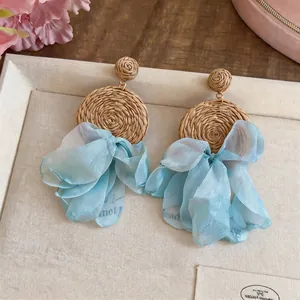 Detailed view of bohemian raffia woven earrings with light blue chiffon ribbons