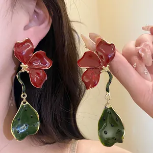 Detailed macro view of retro red flower and green leaf enamel drop earrings with gold edges