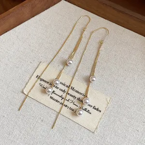 Detail view of elegant 18k gold plated tassel earrings with white pearls on linen