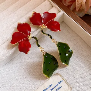 Close-up of exquisite red enamel flower earrings with green leaf pendants and gold accents.