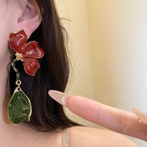 Detailed close-up of vintage red enamel flower and green leaf drop earrings on ear