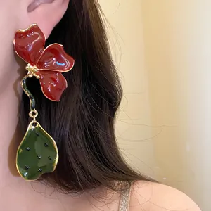 Close-up detail of vintage red enamel flower and green leaf pendant drop earrings