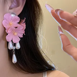 Close-up of pink fabric flower earrings with pearl tassels on a model's ear