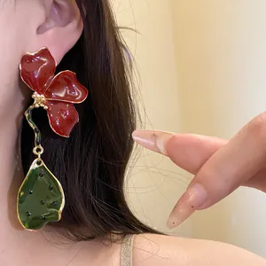 Detailed view of vintage red flower and green leaf enamel drop earrings worn on model's ear