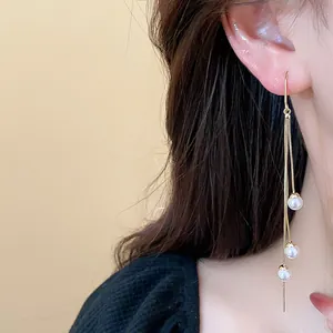 Detailed close-up showing long gold tassel earrings with three delicate white pearls.