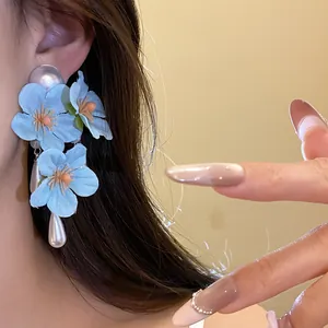 Close-up of elegant blue fabric flower tassel earrings with pearl drops worn on ear.