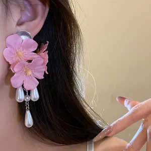 Close-up of elegant pink fabric flower earrings with white pearl tassels worn by a model