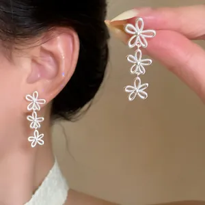 Detailed close-up of silver triple flower dangle earrings worn on a model's ear.