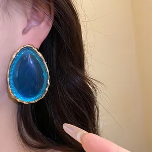 Primo piano di orecchini vintage a goccia in resina blu con bordo dorato testurizzato.