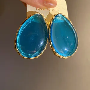 Primo piano di orecchini vintage a goccia in resina blu con bordo dorato testurizzato.