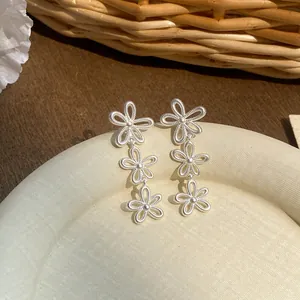 Close-up of elegant silver triple flower dangle earrings on a textured cream plate.