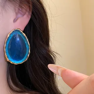 Dettaglio di un orecchino a lobo vintage in resina blu a goccia con bordo dorato