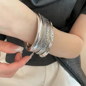 Close-up of silver irregular metal bangles showing matte and hollow textures on wrist.