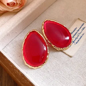 Primo piano di orecchini vintage in resina rossa con montatura dorata testurizzata.
