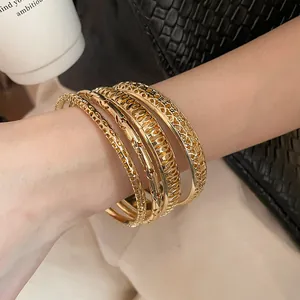 Macro detail showing a stack of elegant golden hollowed-out metal bangles on a wrist