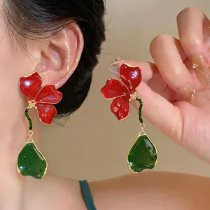 Gros plan de boucles d'oreilles fleurs en émail rouge et vert avec bordure dorée.