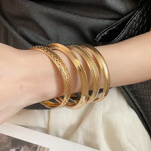 Close-up detail of four textured gold metal bangles elegantly styled on a model's wrist