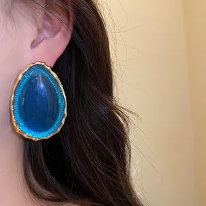 Eleganti orecchini a goccia in resina blu con cornice dorata martellata in primo piano