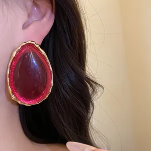 Primo piano di un orecchino a goccia in resina rosso-rosa con bordo dorato martellato